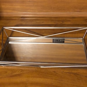 May include: A silver metal tray with a mirrored surface. The tray has a geometric design and is perfect for displaying small items.