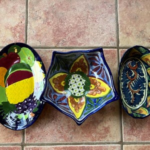 May include: Three colorful ceramic bowls with intricate designs. The bowls are blue, yellow, green, and red with floral patterns. The bowls are on a tiled surface.