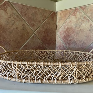 May include: A woven oval tray with two handles. The tray is made of natural wicker and has a light brown color.