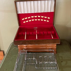 May include: A wooden storage chest with a hinged lid, featuring a red velvet interior lining with white satin accents and slots for cutlery. In front of the chest sits a rectangular, silver-toned metal wire rack with multiple dividers.