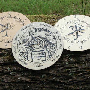 May include: Three wooden clocks with different designs. The first clock features a tree with the inscription "The One Ring" in Elvish script. The second clock features a drawing of a hobbit hole with the inscription "Second Breakfast" in Elvish script. The third clock features the inscription "The One Ring" in Elvish script and the symbol for the One Ring.