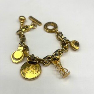 Peut inclure: Un bracelet à breloques en or avec une variété de breloques, dont un breloque rond avec un motif, un breloque en forme de cœur, un petit breloque en forme de boule et un breloque avec un anneau. Le bracelet est fait d'une épaisse chaîne en or.