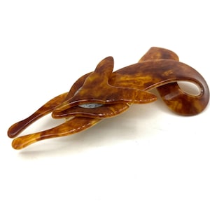 Peut inclure: Une pince à cheveux à motif écaille de tortue avec un design abstrait et fluide. La pince présente une série de formes incurvées et de pointes allongées, créant un accessoire dynamique et élégant. La couleur est un mélange chaleureux de brun et d'ambre.