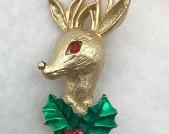 May include: Gold-tone reindeer brooch with red rhinestone eyes and a green holly sprig with red berries.