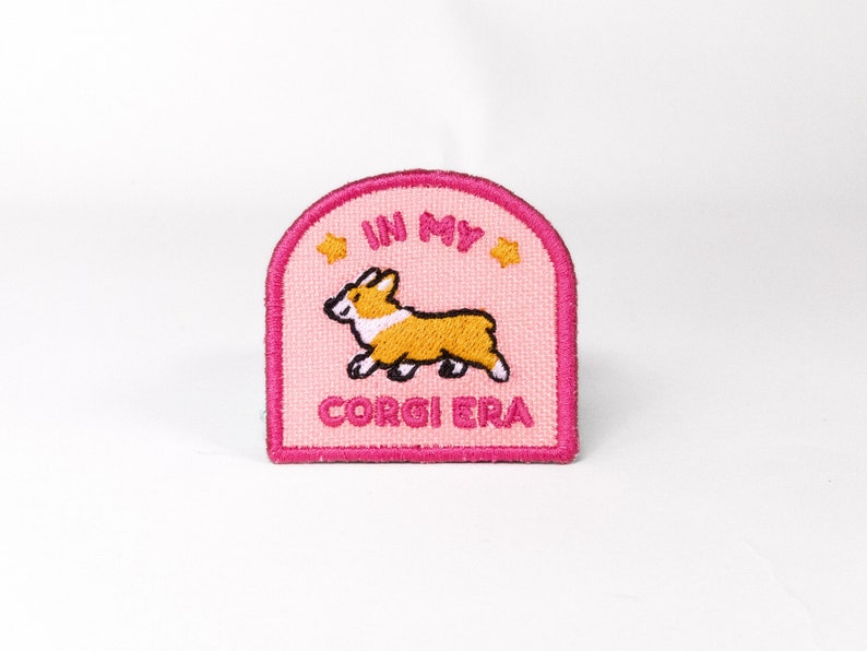 May include: Pink and white embroidered patch with a cartoon corgi and the text "In My Corgi Era".