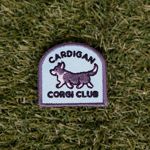 May include: A light blue embroidered patch with a black and white cartoon Cardigan Welsh Corgi walking. The patch says "Cardigan Corgi Club" in black embroidery.