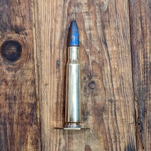 以下が含まれることがあります： 木製の表面に置かれた、青い先端を持つ金色の弾丸1つ