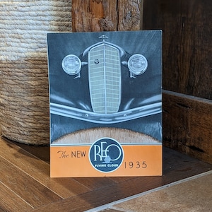 Peut inclure: Une publicité vintage pour la voiture Reo Flying Cloud de 1935. La publicité présente une image en noir et blanc de l'avant de la voiture avec le logo Reo et le texte "The New Reo Flying Cloud 1935".