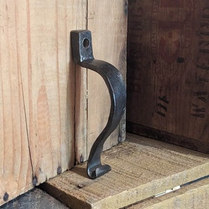 Peut inclure: Poignée en métal noir avec un design incurvé, fixée à une boîte en bois.