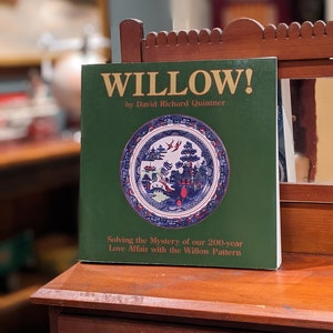 Puede incluir: Un libro verde titulado "WILLOW!" de David Richard Quintner. La portada del libro presenta un plato con un patrón de sauce azul y blanco y el texto "Solving the Mystery of our 200-year Love Affair with the Willow Pattern."