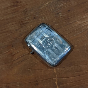 Puede incluir: Un portacerillas de plata con un diseño grabado. El portacerillas está sobre una superficie de madera.