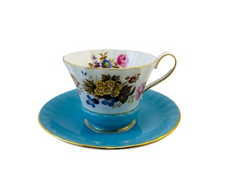 May include: A white teacup and saucer with a floral pattern and a turquoise blue rim. The saucer has a gold trim.