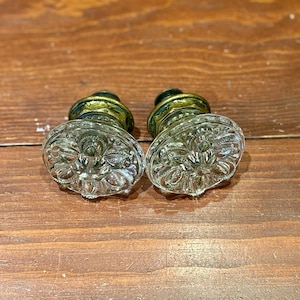 May include: Two antique glass door knobs with ornate designs and brass accents. The knobs are oval shaped and have a clear glass finish.