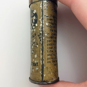 Puede incluir: Una peque&ntilde;a lata redonda de color marr&oacute;n con letras blancas. La lata est&aacute; etiquetada como "Durable Tire Tape" y tiene instrucciones de uso. La lata est&aacute; siendo sostenida por una mano.