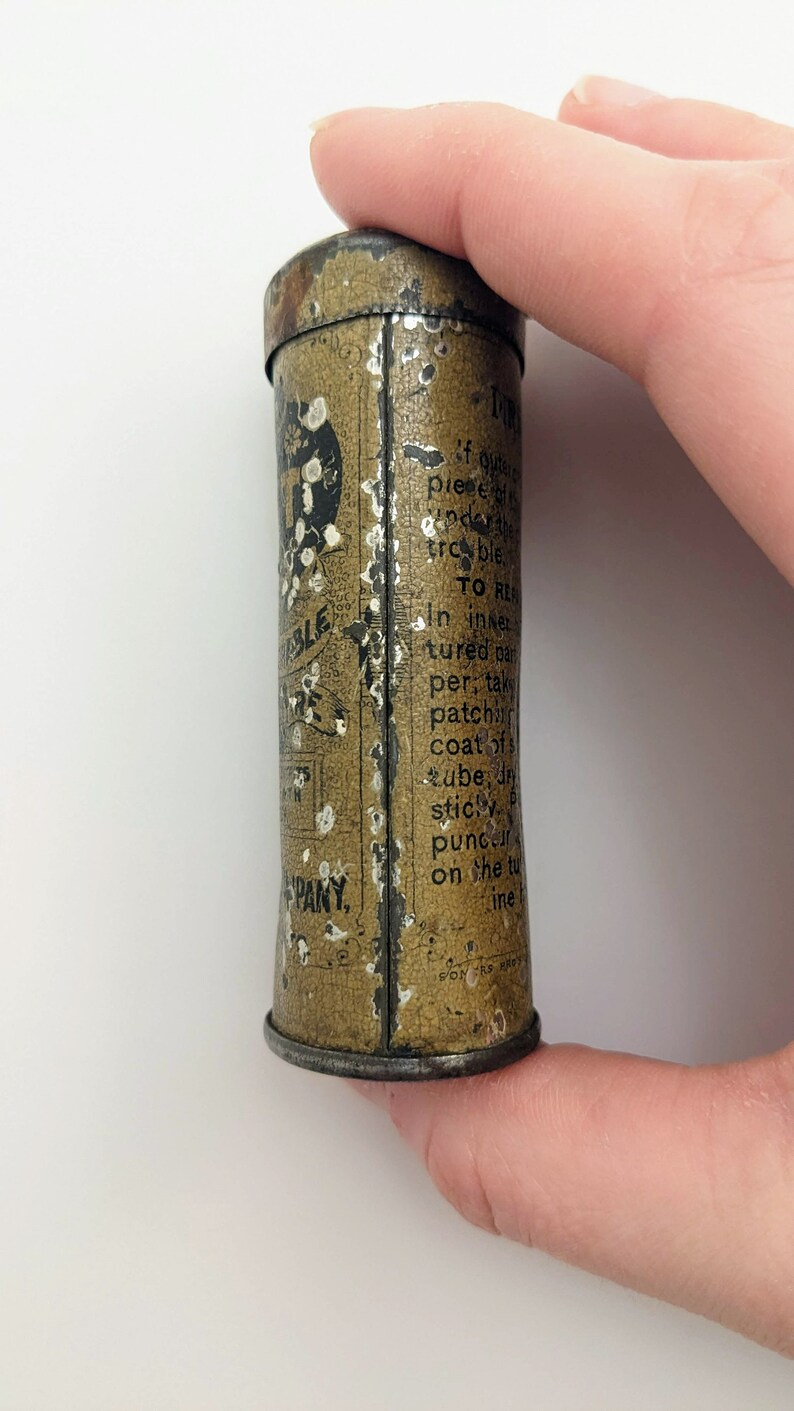 Puede incluir: Una peque&ntilde;a lata redonda de color marr&oacute;n con letras blancas. La lata est&aacute; etiquetada como "Durable Tire Tape" y tiene instrucciones de uso. La lata est&aacute; siendo sostenida por una mano.