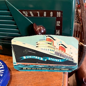 May include: A vintage advertisement for 85 best gold eyed needles and needle threader. The ad features a blue and white illustration of a ship called "United States" with the text "85 Best Gold Eyed Needles and Needle Threader" and "Loft Knit The Pioneer Moose Co. St. Louis, Mo."