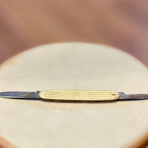 Może przedstawiać: Mały, złoty scyzoryk z dwoma ostrzami. Scyzoryk ma teksturowany uchwyt i jest zamknięty.