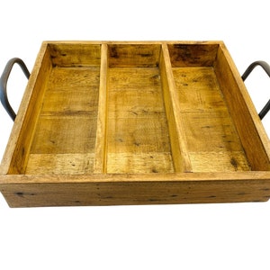 Puede incluir: Una bandeja de servir de madera con tres compartimentos divididos y asas de metal negro. La bandeja está hecha de madera natural con un acabado marrón claro.