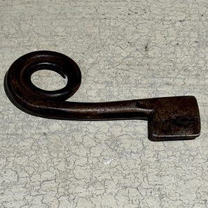 May include: A dark brown metal key with a unique spiral design at the top and a flat, rectangular blade.