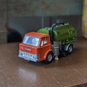 Pode incluir: Um caminhão de brinquedo vermelho e verde com uma mangueira de vácuo e uma placa de matrícula FTR 47N. O caminhão é uma varredeira de ruas.