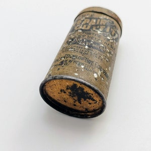 Puede incluir: Un contenedor de hojalata vintage para un kit de reparaci&oacute;n de neum&aacute;ticos. La lata es marr&oacute;n con salpicaduras de pintura blanca y texto negro que dice "Tire Repair Outfit for the Detachable Hose Sold in Pairs of 12".