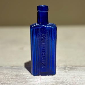 May include: A cobalt blue glass bottle with a ribbed design and the text "PHOL. SUL." embossed on the front.