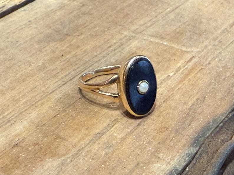 Peut inclure: Bague dor&eacute;e orn&eacute;e d'une pierre ovale bleu fonc&eacute; avec un petit accent blanc rond. La bague a un design &agrave; anneau fendu. Bijoux.