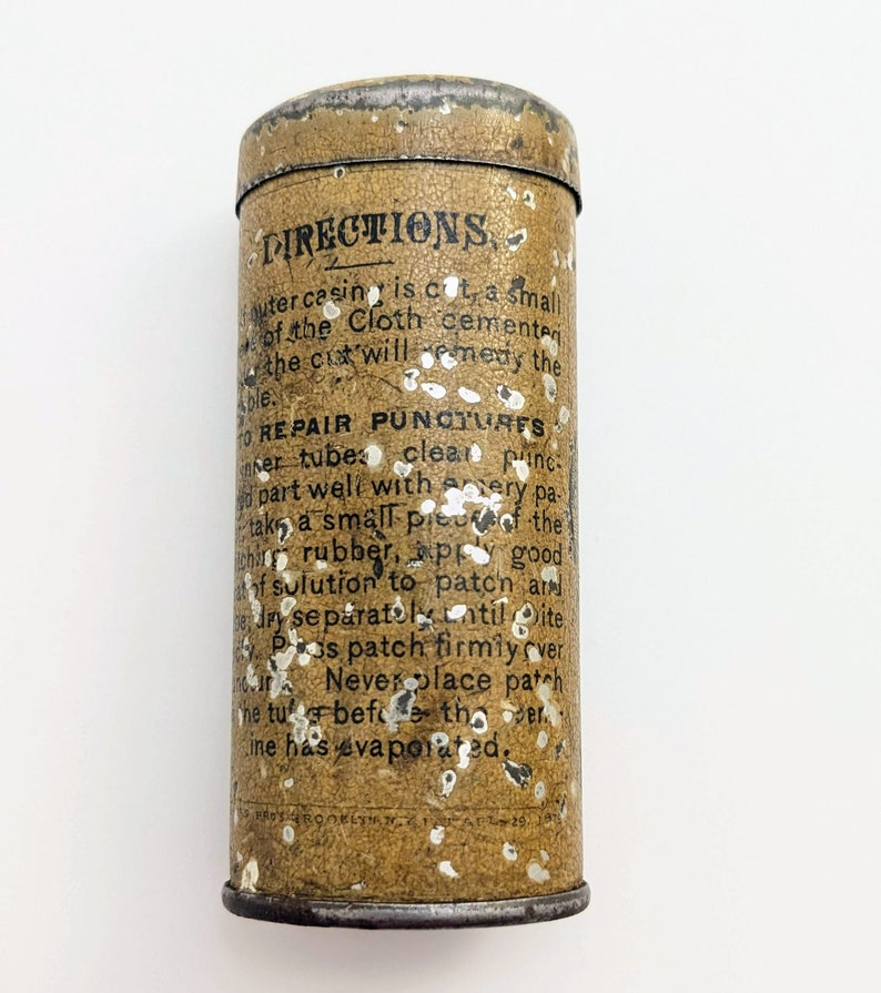 Puede incluir: Una lata vintage de metal con una superficie moteada de marr&oacute;n y blanco. La lata tiene una etiqueta negra con el texto "DIRECTIONS" e instrucciones para reparar pinchazos. El texto est&aacute; en negro con un contorno blanco.