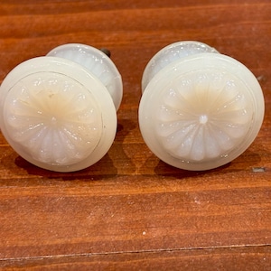 May include: Two white glass cabinet knobs with a floral design. The knobs have a raised, textured flower pattern in the center.