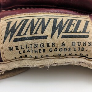Puede incluir: Primer plano de un guante de cuero marr&oacute;n con una etiqueta blanca que dice "Winn Well Wellinger & Dunn Leather Goods Ltd. Toronto Canada".