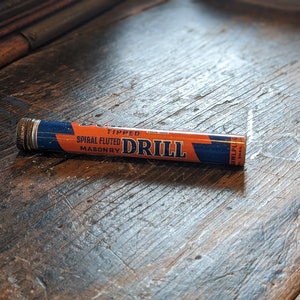 May include: A blue and orange drill bit container with the text "Tipped Spiral Fluted Masonry Drill" on it.