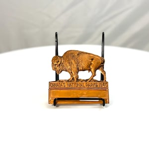Puede incluir: Figura de bisonte de madera marrón sobre un soporte de metal negro. El bisonte tiene detalles de pelaje y se encuentra sobre una base rectangular con el texto "CANADA'S NATIONAL PARKS 1940".