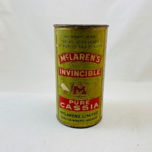 Könnte beinhalten: Eine vintage grüne und rote Blechdose mit der Aufschrift "McLaren's Invincible Pure Cassia" und einem großen "M"-Logo. Die Dose ist 1 1/2 Unzen schwer und trägt den Schriftzug "The Quintessence of Purity and Flavor".