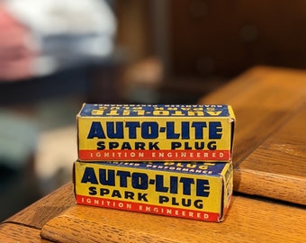 Peut inclure: Deux boîtes de bougies d'allumage Auto-Lite vintage empilées l'une sur l'autre. Les boîtes sont jaunes avec des lettres bleues et portent les mots "Auto-Lite Spark Plug" et "Ignition Engineered" imprimés dessus.