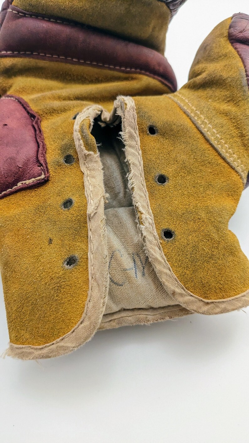 Puede incluir: Un par de guantes de boxeo de cuero marr&oacute;n con un exterior de gamuza beige. Los guantes tienen un forro blanco y una inscripci&oacute;n manuscrita que dice "CM".