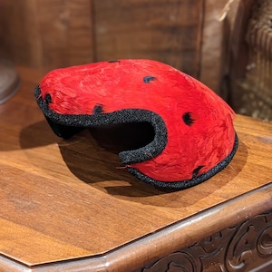 May include: A red feather hat with black trim and black polka dots. The hat is sitting on a wooden table.