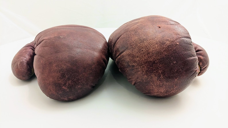 Puede incluir: Un par de guantes de boxeo de cuero marr&oacute;n. Los guantes est&aacute;n usados y tienen un aspecto desgastado.