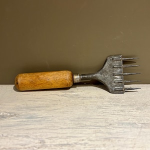 May include: An antique ice pick with a wooden handle and a metal head with multiple sharp prongs. The handle is a light brown color, and the metal head has a silver finish. The tool is designed for breaking ice.