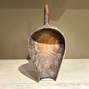 May include: A wooden scoop with a handle, made from dark wood with a worn finish. The scoop is empty and has a rounded shape.