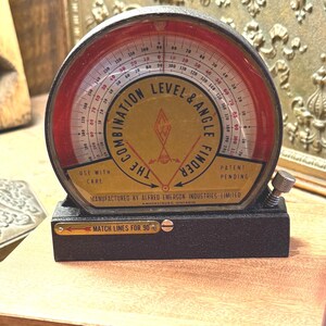 Könnte beinhalten: Ein schwarzer Kombinations-Wasserwaagen- und Winkelmesser aus Metall mit einer halbkreisförmigen roten und gelben Skala. Das Zifferblatt zeigt den Text THE COMBINATION LEVEL & ANGLE FINDER, USE WITH CARE, PATENT PENDING und MANUFACTURED BY ALFRED EMERSON INDUSTRIES LIMITED.