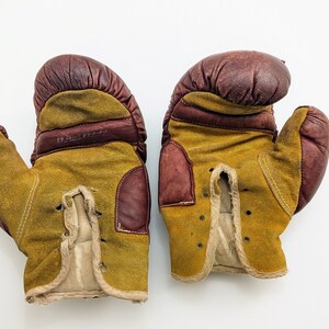 Puede incluir: Un par de guantes de boxeo vintage de cuero marr&oacute;n y gamuza amarilla. Los guantes tienen cordones y est&aacute;n desgastados.