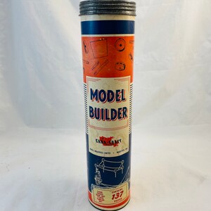 Op de afbeelding: Een blauwe en witte kartonnen buis met een zilveren deksel. De buis bevat een modelbouwset genaamd "Model Builder" van Cana-Craft. Het etiket zegt "Bevat 137 stukken".