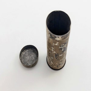 Puede incluir: Un contenedor de hojalata vintage con un dise&ntilde;o estampado en blanco y negro. El contenedor est&aacute; abierto y la tapa est&aacute; sentada a su lado. El contenedor est&aacute; hecho de metal y tiene un aspecto ligeramente desgastado.