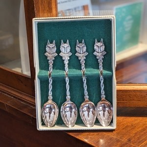 May include: Set of four silver teaspoons with fox head handles in a white box with a green velvet lining. The fox heads are detailed with the words "Wolf Cubs" on each.