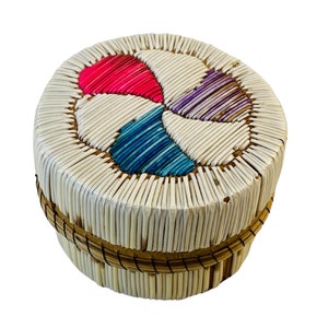 May include: A round, woven basket with a white base and a colourful geometric design on the top. The design is made of pink, blue, and purple feathers.