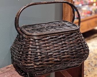 May include: A dark brown wicker basket with a hinged lid and a single handle. The basket is sitting on a wooden stool.