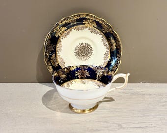 May include: A white teacup and saucer with a blue and gold floral design. The saucer has a scalloped edge.