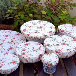 May include: Set of eight reusable food covers in a floral pattern with pink, red, and yellow flowers on a white background. The covers are made of fabric and are designed to fit over bowls and containers to keep food fresh.