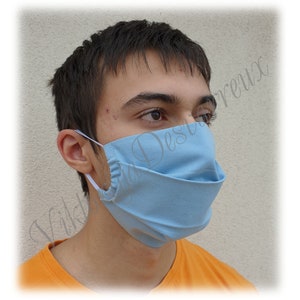May include: A person wearing a light blue face mask. The mask is made of fabric and has a pleated design.