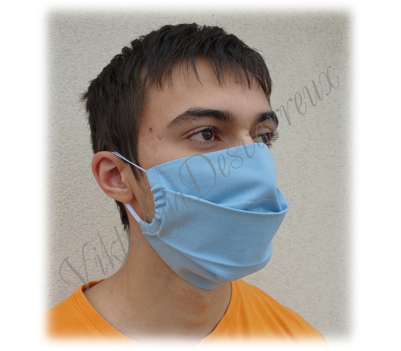 May include: A person wearing a light blue face mask. The mask is made of fabric and has a pleated design.